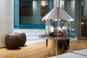 Rondo Classic en stilfull rund eldstad i rostfritt stål placerad framför en pool i en elegant spaanläggning